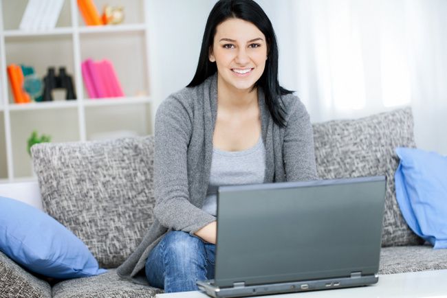 Morning, young girl with laptop computer, sitting in bright living room, looking at camera.